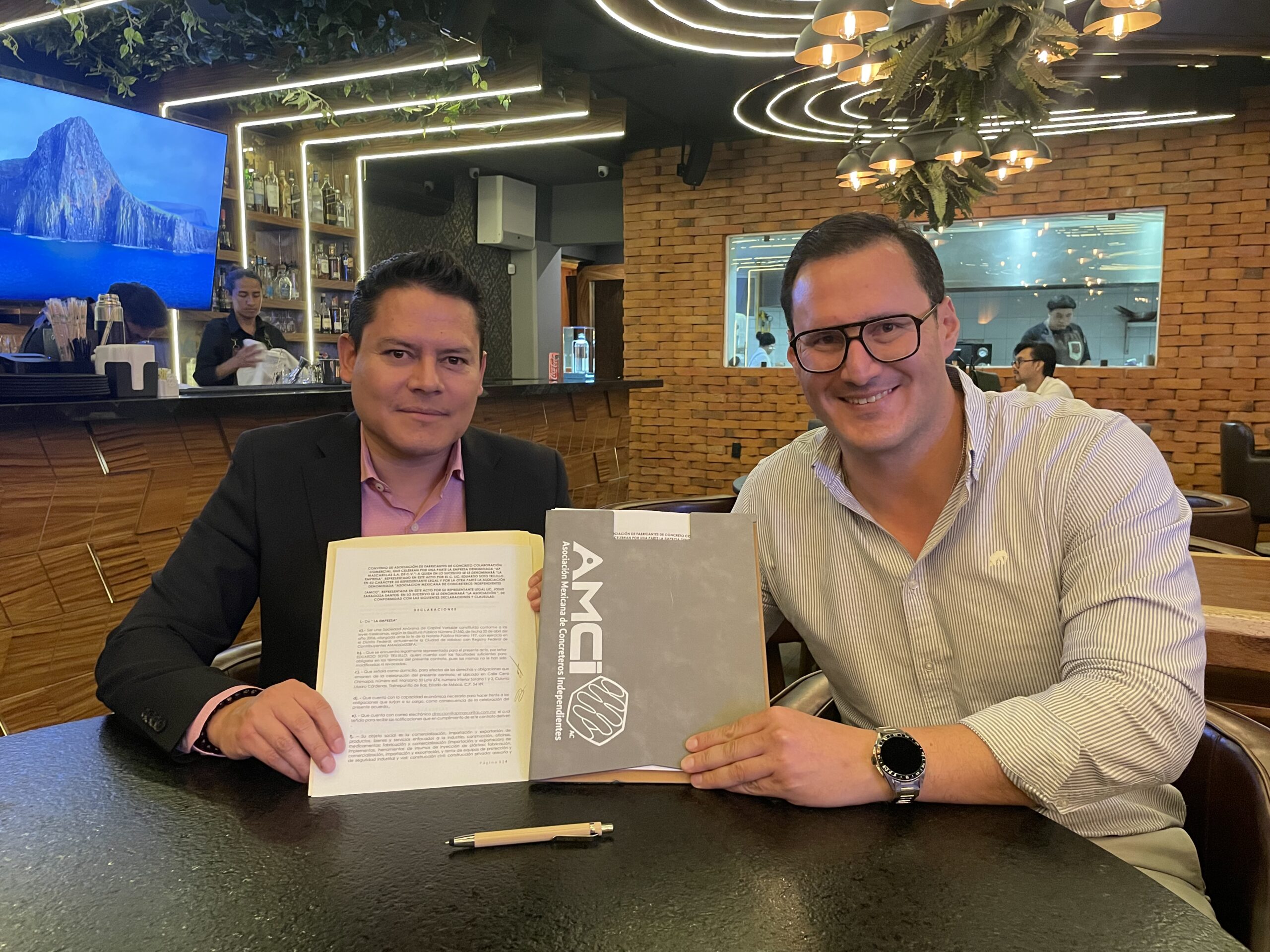 Dos personas muestran un documento y una carpeta con el logo de AMCI durante una reunión.